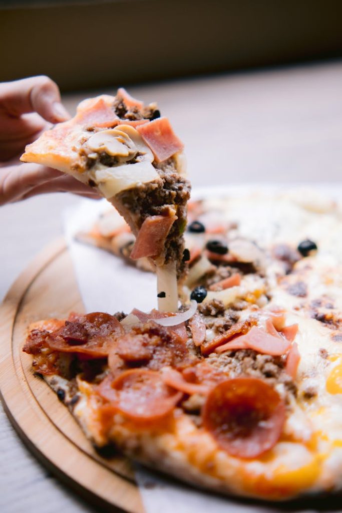 Close-up of a fresh artisan pizza slice being lifted from a wooden platter.