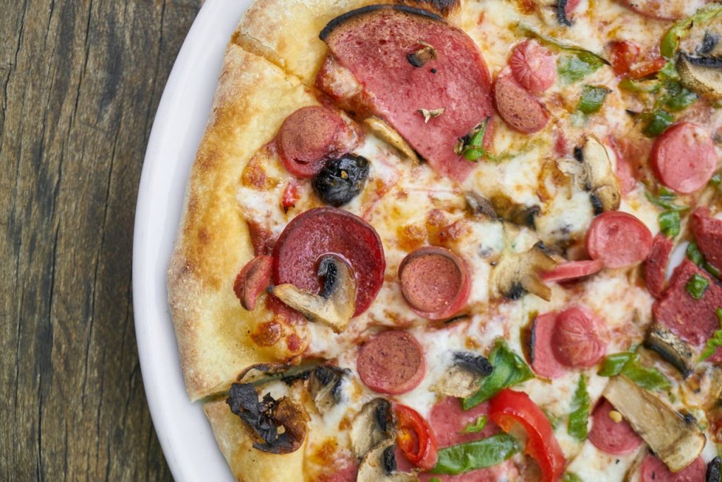 A delicious slice of pepperoni pizza topped with mushrooms and peppers on a rustic wooden surface.